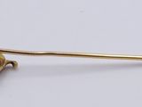 a gold pin with a ball on it on a white surface