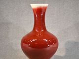 un vase rouge posé sur une table, sur fond gris