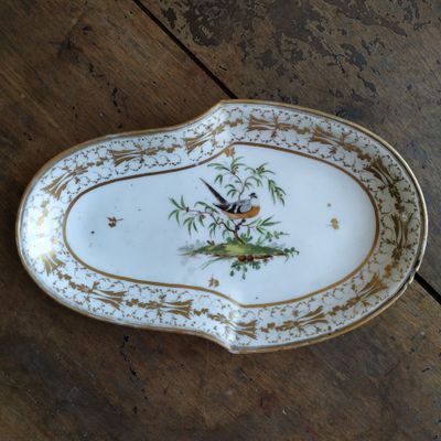 une assiette sur laquelle est représenté un oiseau, posée sur une table en bois