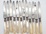 six silverware knives with mother of pearl handles on a white surface