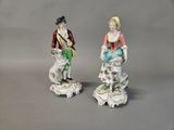 pair of porcelain figurines of a man and a woman with a dog