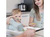 a woman feeding a baby with a spoon in a high chair