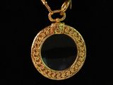 a close up of a gold necklace with a black glass on it
