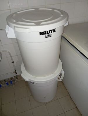 une poubelle blanche posée dans une salle de bains, à côté d'une machine à laver
