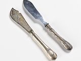 pair of silver plated cheese knives and a knife on a white surface