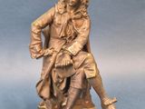 statue en bronze représentant un homme assis sur une chaise, les jambes croisées