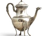 an antique silver teapot with a peacock handle on a stand