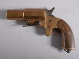 un vieux revolver en laiton avec une crosse en bois, posé sur une surface blanche