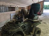 a green atv parked in a barn with a bucket on the back of it