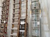 Plusieurs échelles en bois sont alignées contre un mur dans un entrepôt.