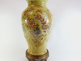 a yellow vase with flowers on it sitting on a stand