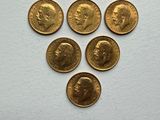 six gold sovereigns of different sizes and shapes on a white surface