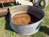 un grand seau en métal posé dans l'herbe à côté d'un tas de pneus
