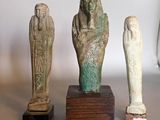 four ancient egyptian statues are displayed on a table in front of a white wall