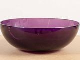 purple glass bowl sitting on top of a wooden table next to a white wall