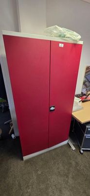 a red cabinet in the corner of a room next to a desk