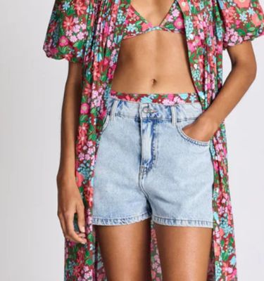 a woman in a floral top and denim shorts stands in front of a white background