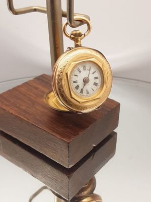 une horloge en or posée sur un socle en bois, elle-même posée sur une table en verre