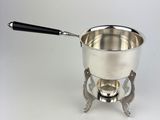 a silver pot with a black handle on a saucer