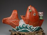 une photo représentant une statue de poisson rouge et vert posée sur un socle en bois