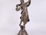 une statue antique en bronze représentant une femme tenant un oiseau, posée sur un socle