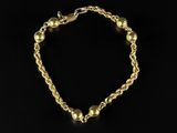a gold chain bracelet with beads on a black background
