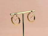 une paire de boucles d'oreilles créoles en or posées sur un présentoir en or
