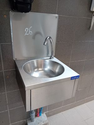 un lavabo en acier inoxydable dans des toilettes publiques, avec un distributeur de serviettes en papier fixé au mur