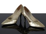 une paire de chaussures dorées posées sur une surface noire, sur fond blanc