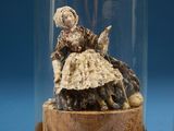 two miniature figurines of a woman in a dress under a glass dome