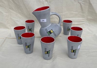 six cups and a pitcher on a table with a white cloth