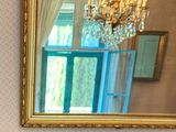 a mirror with a gold frame and a chandelier hanging from it