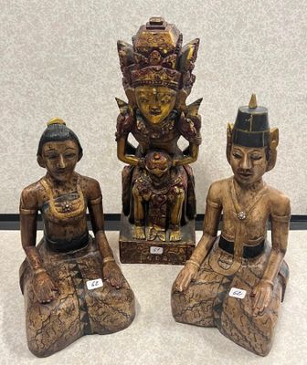 trois statues en bois représentant des personnes assises sur une surface blanche