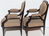 pair of antique chairs with upholstered arms and foot rests against a white wall