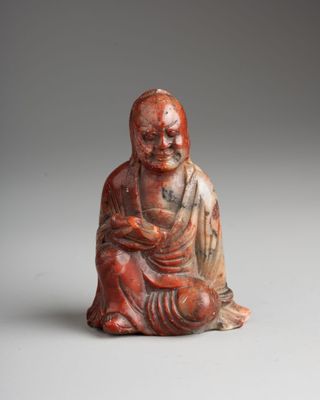 une petite statuette rouge et blanche représentant un Bouddha assis