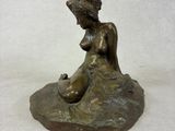 bronze statue of a woman sitting on a rock with a hat on her head