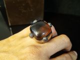 a person ' s hand holding a ring with a brown stone on it