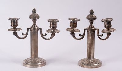 une paire de bougeoirs plaqués argent sur des socles, sur fond blanc