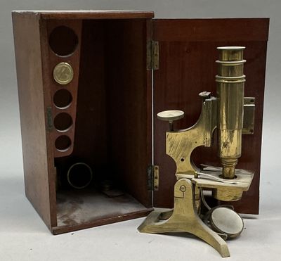 un microscope ancien en laiton, dans un coffret en bois, posé sur une surface blanche