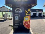 un distributeur automatique sur lequel est posée une pizza, dans un parking