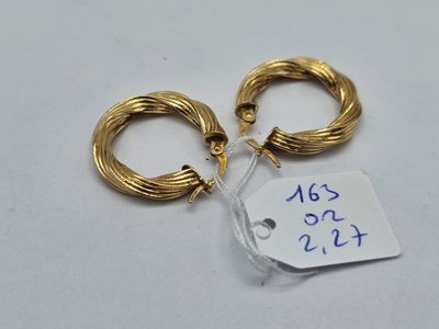 deux boucles d'oreilles en anneau dorées, avec une étiquette de prix, posées sur une surface blanche