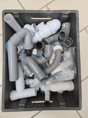 a box full of plastic pipes and fittings on a tiled floor
