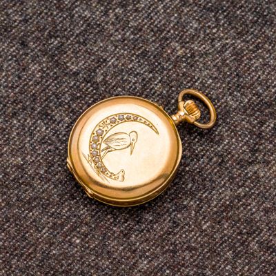 une image représentant une montre de poche en or sur laquelle figure un oiseau