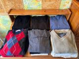 several sweaters are arranged on a wooden bench in front of a wall