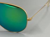 lunettes de soleil à monture dorée et verres verts miroités, sur fond blanc