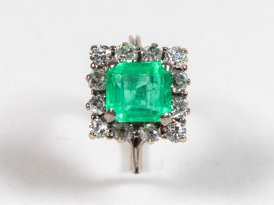un gros plan d'une bague sertie d'une émeraude verte et de diamants, posée sur une surface blanche