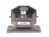 une horloge en argent posée sur un socle, sur une surface blanche