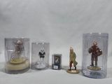 cinq figurines miniatures dans des vitrines, posées sur un fond blanc