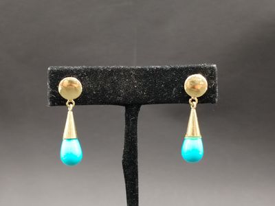 une paire de boucles d'oreilles turquoise et or posées sur un présentoir noir