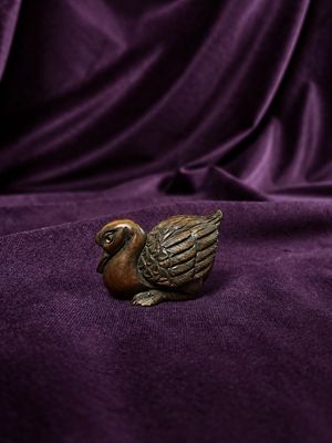 a small bronze duck figurine sitting on a purple cloth